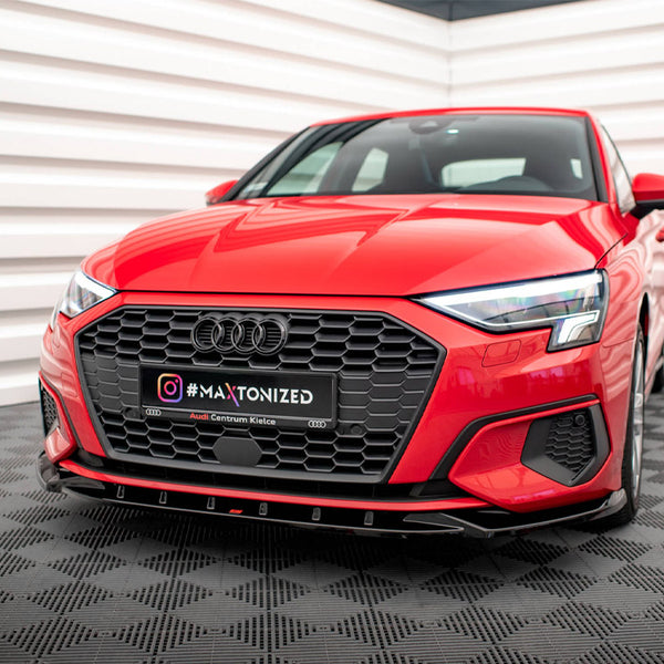 A red car is stationary in a showroom with textured flooring and white paneled walls. The license plate reads "#MAXTONIZED Audi Centrum Kielce" alongside the Instagram logo.