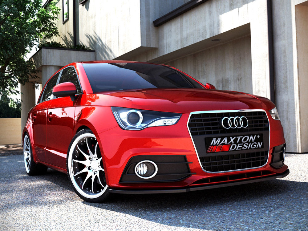 A red Audi car is parked on a sunlit street in front of modern buildings. The license plate reads "MAXTON DESIGN." Shadows and trees are visible nearby.