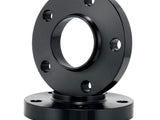A black, circular metal flange with bolt holes is stacked on another identical flange. The object rests on a plain white background, highlighting its industrial design and smooth finish.