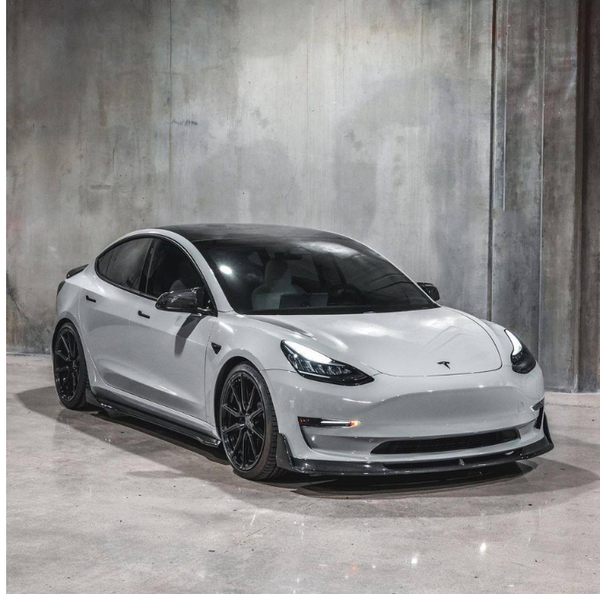 A sleek, white car with black wheels is parked in an industrial-style setting with plain, textured concrete walls and floor.
