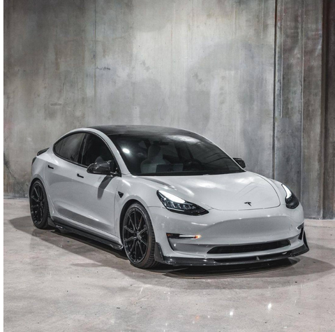 A sleek, white car with black wheels is parked in an industrial-style setting with plain, textured concrete walls and floor.
