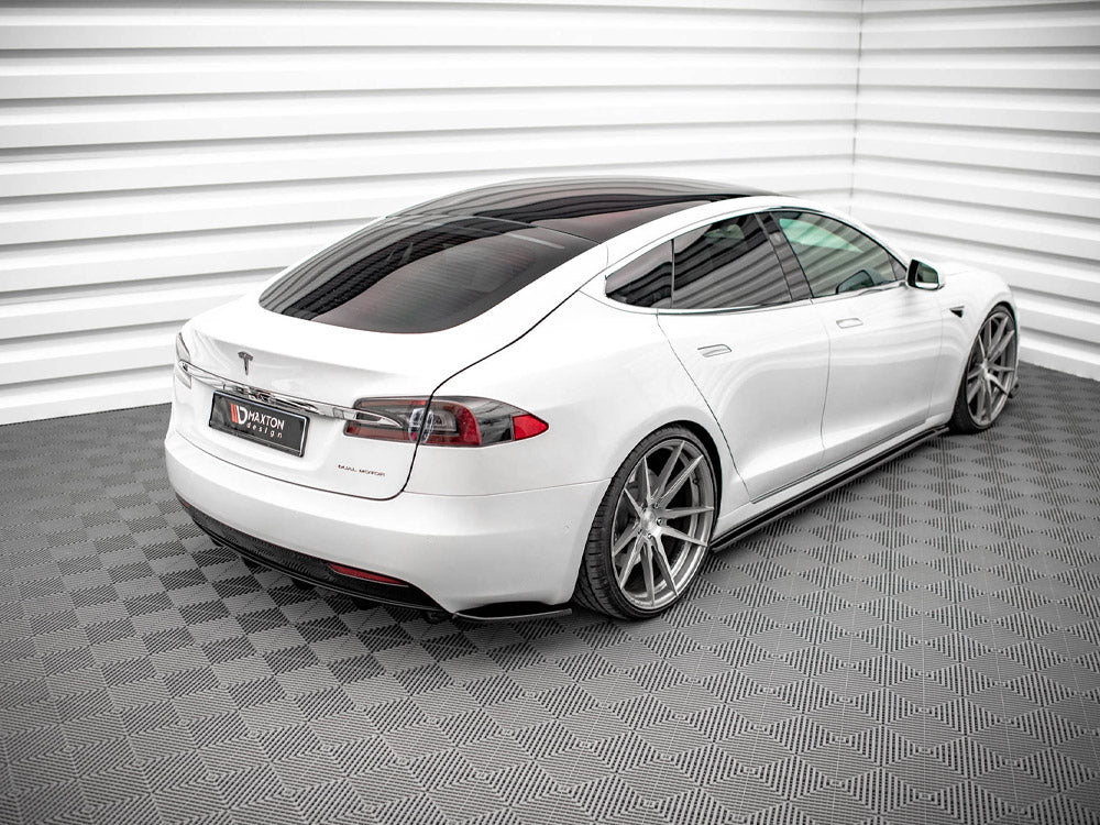 A white car with tinted windows is parked in a room with textured flooring and ridged walls. A license plate displays the text "MAXTON DESIGN."