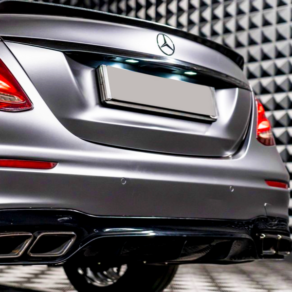 A silver luxury car's rear, with a visible logo and tail lights, is parked in an acoustically insulated room featuring a textured, geometric wall pattern.