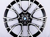 A black and chrome car wheel rim, with intricate geometric patterns, displaying the BMW logo at its center; set against a plain white background.