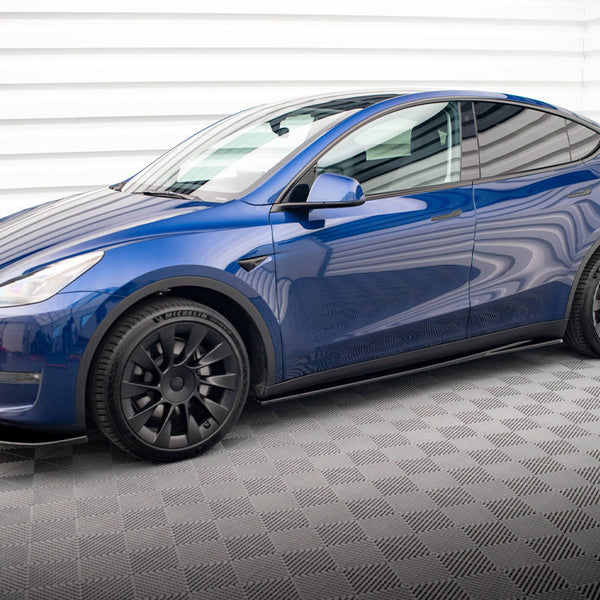 A blue electric car is stationary in an indoor garage with patterned flooring and white paneled walls, featuring black wheels and sleek, modern design lines.