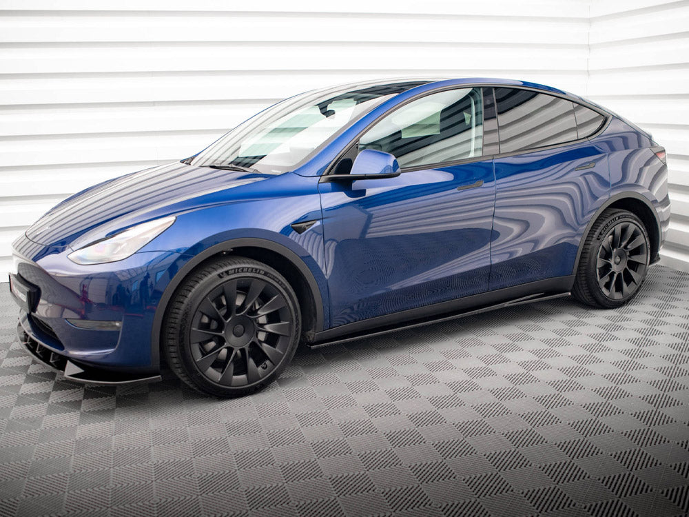 A blue electric car is stationary in an indoor garage with patterned flooring and white paneled walls, featuring black wheels and sleek, modern design lines.
