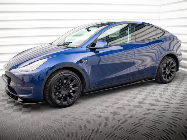A blue electric car is stationary in an indoor garage with patterned flooring and white paneled walls, featuring black wheels and sleek, modern design lines.