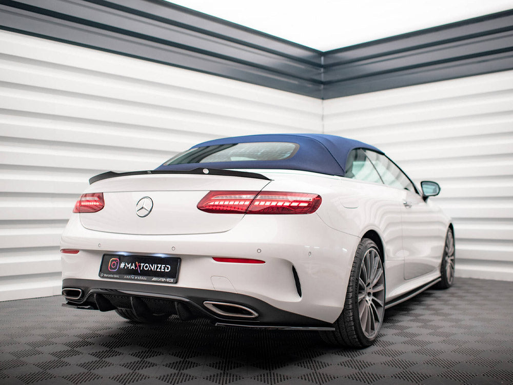 A white convertible car with a blue top parked in a bright, modern showroom with checkered flooring. Text on the license plate reads, “MaxTonized” with social media icon and AMG branding.