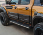 A modified pickup truck, parked, displaying a shiny orange and black exterior with large off-road tires labeled "BFGoodrich" and distinct side steps; situated on a paved surface.