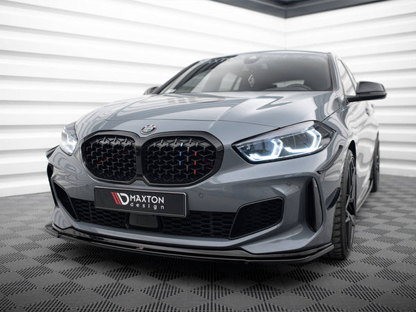 A sleek, grey BMW car with illuminated headlights sits on a checkered floor in a modern, white-panelled room. The license plate reads "MAXTON design."