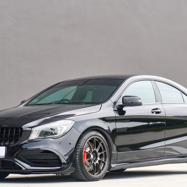 A sleek black car is parked on a smooth surface, featuring shiny black wheels. It is positioned against a plain gray wall, with buildings visible in the background.