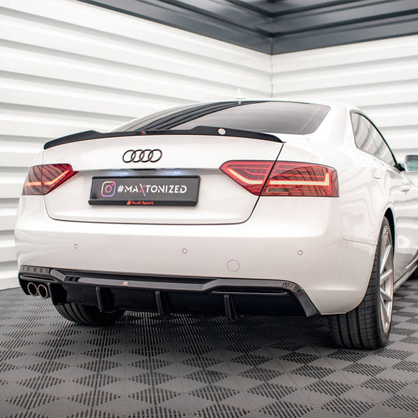 A white Audi car is parked in a garage with patterned flooring and white walls. The license plate reads "#MAxtonized" with "Audi Sport" below it.