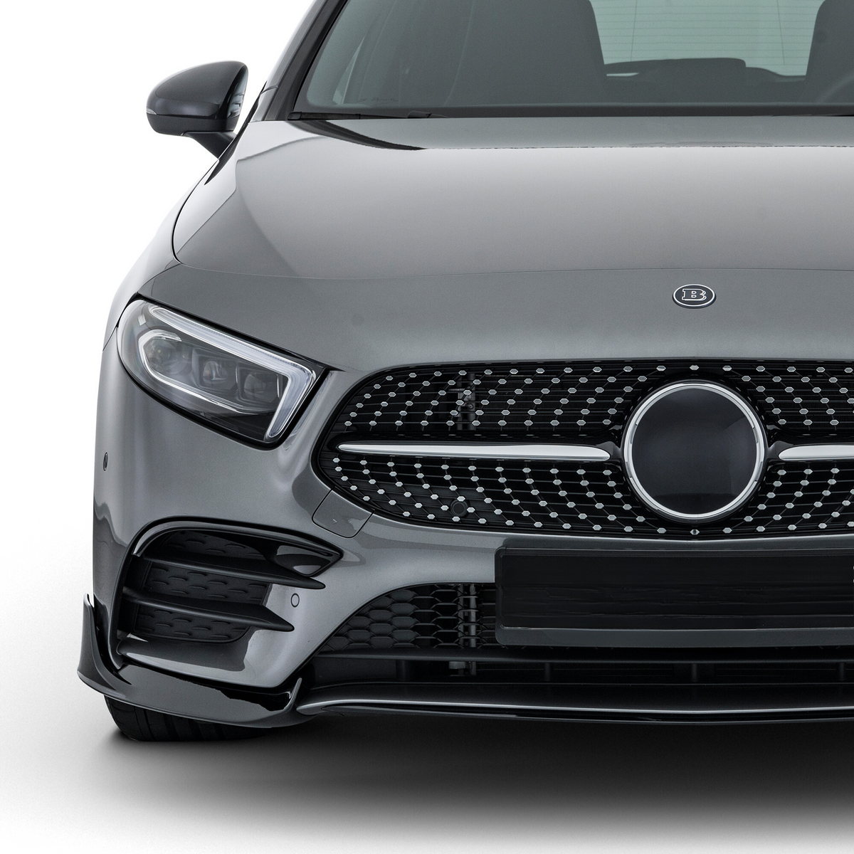 A gray luxury car is parked, showcasing its sleek front grille with a circular emblem. The vehicle sits in a well-lit studio environment, highlighting its polished exterior.
