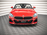 A red convertible sports car sits stationary on a patterned floor within a white-walled room. Its front grille prominently displays the BMW logo. Text on the bumper reads 