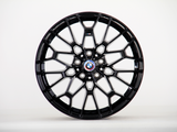 A black alloy wheel with a geometric spoke design, emblazoned with the BMW logo at the center, stands against a plain white background.