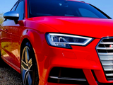 A red sports car with sleek headlights is parked on gravel, under a clear blue sky. The car's distinctive grille and angular design suggest high performance and modern styling.