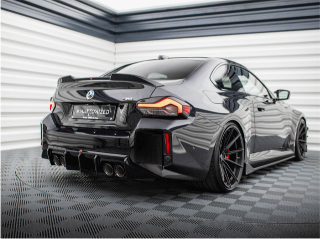 A sleek black sports car is parked in a modern, checkered-floor showroom. The license plate reads "#MAXTONIZED". The car features a glossy exterior and quad exhaust pipes.