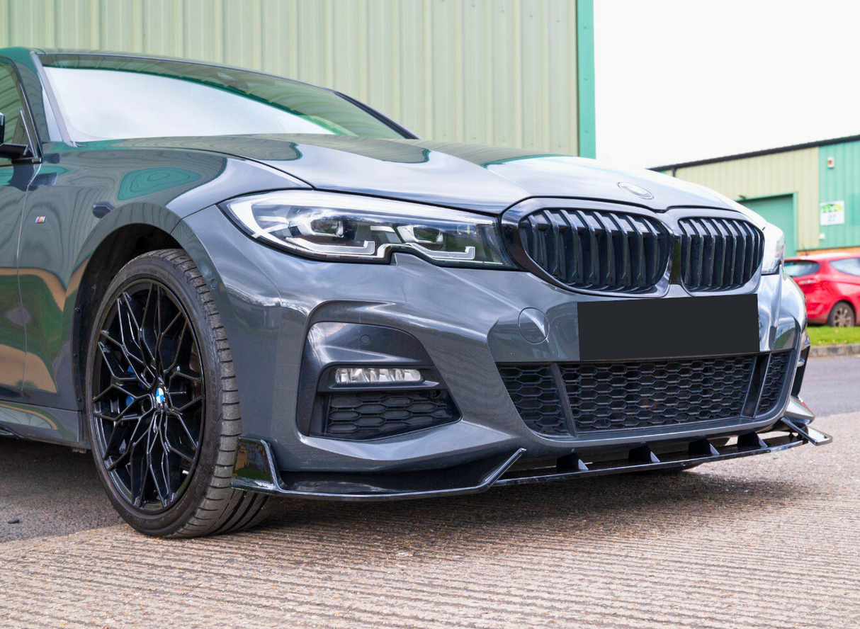 A sleek grey car with a distinctive grille and black alloy wheels is parked on a textured surface, with green industrial buildings in the background.