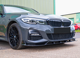 A sleek grey car with a distinctive grille and black alloy wheels is parked on a textured surface, with green industrial buildings in the background.