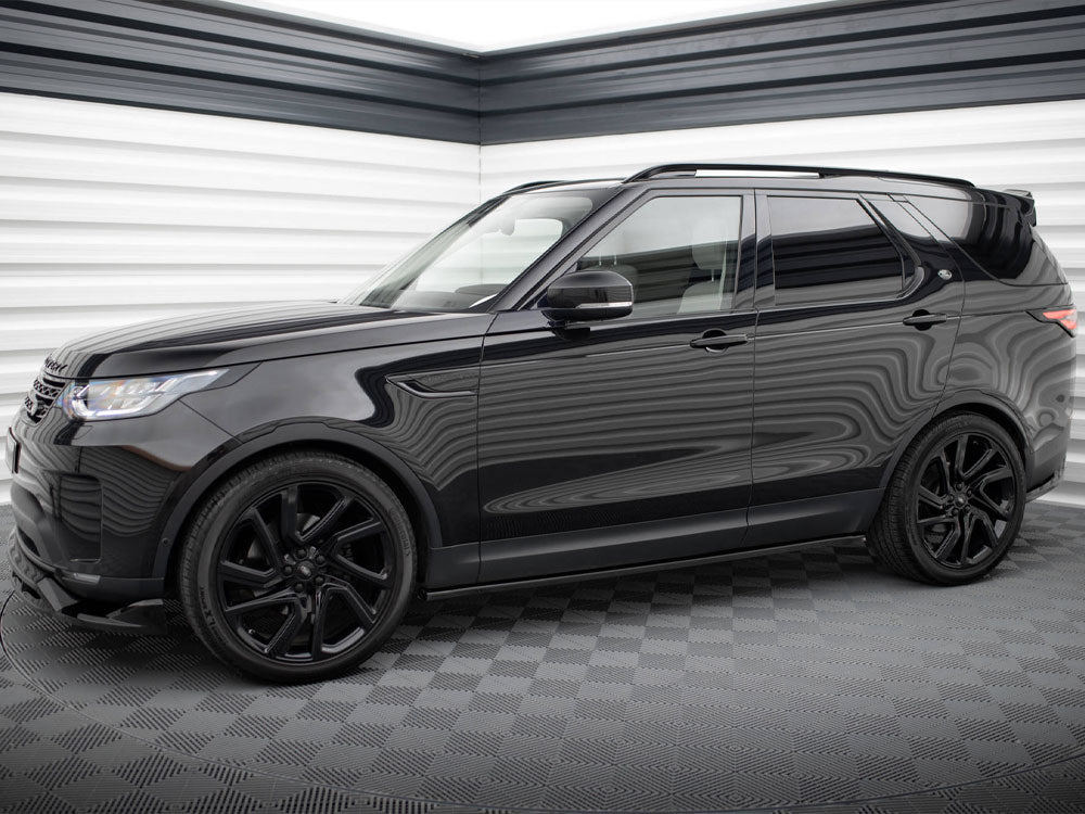 A black SUV is parked in a garage with checkered flooring and striped walls, reflecting light off its glossy surface.