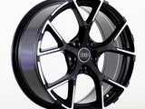 A glossy black alloy wheel with a five-spoke design is standing upright. It features the Audi logo at the center, against a plain white background.