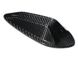 A sleek, black carbon fiber object sits on a white background, showcasing a smooth, aerodynamic shape with a woven texture, possibly designed for vehicle use or aerodynamics.