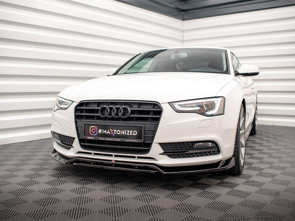 A white Audi car parked on a checkered floor in a cornered space. The license plate reads "#MAXTONIZED" with Instagram logo.
