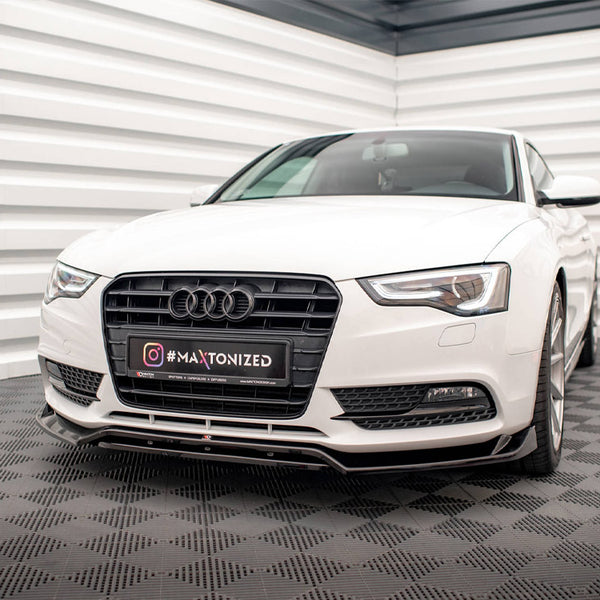 A white Audi car parked on a checkered floor in a cornered space. The license plate reads "#MAXTONIZED" with Instagram logo.