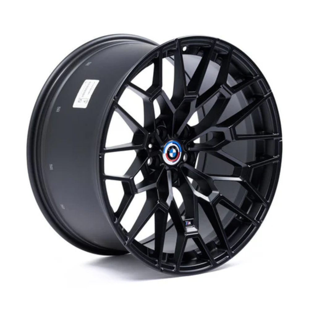 A sleek, black alloy wheel with an intricate, angular spoke design features a central emblem. It rests standing on a white background.