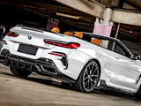 Convertible BMW car, parked, in a dimly lit concrete parking garage. The car is white with notable rear design details and black, sporty wheels. A 