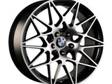 A multi-spoke alloy wheel with geometric patterns features the BMW logo at the center. It has a metallic finish and is designed for automotive use.
