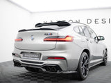 A silver BMW X4 M, featuring a rear spoiler and quad exhausts, is stationary on a checkered platform. Visible text includes 