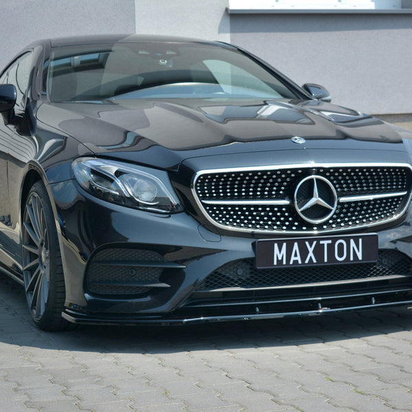 A black Mercedes-Benz car is parked on a paved surface, featuring a prominent grille with a star emblem. The license plate reads "MAXTON," and it's beside a modern building.