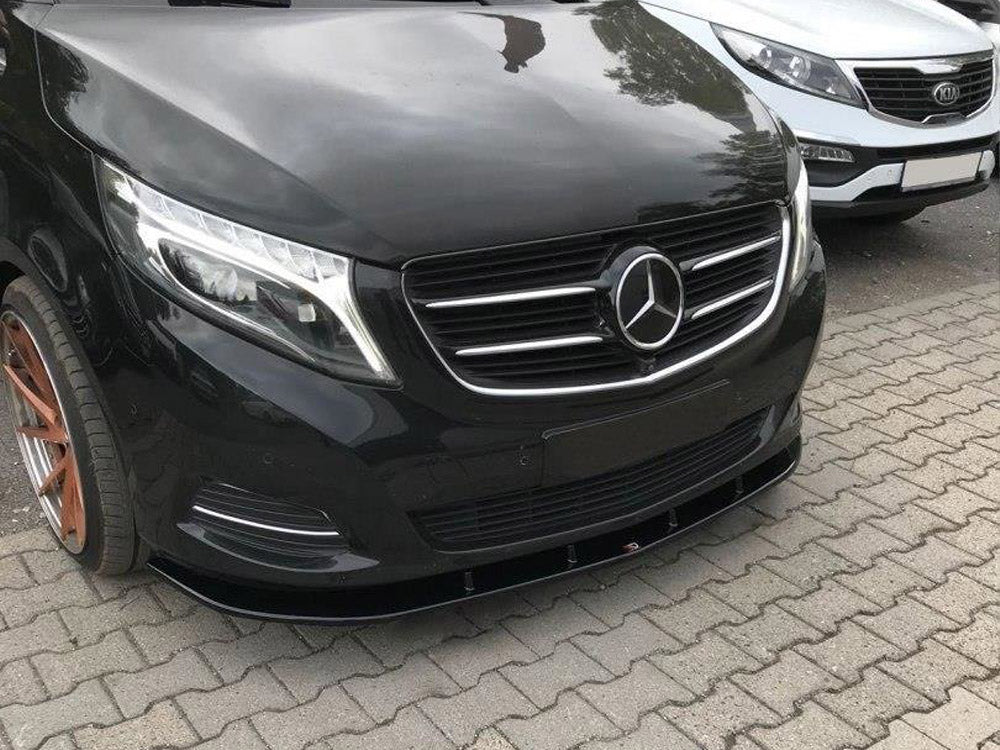 A black Mercedes-Benz vehicle is parked on a paved surface alongside a white Kia, in an outdoor setting. The Mercedes emblem is prominently displayed on the grille.