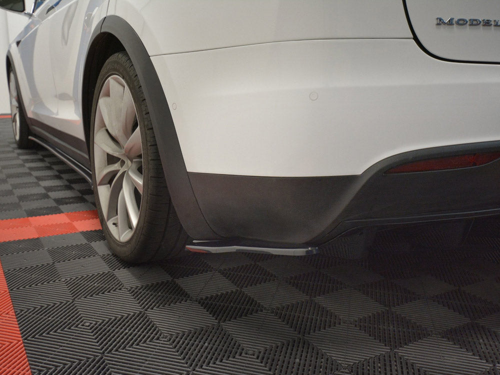 A white car's rear section is parked on a checkered black and red floor. The car is stationary, with visible rear wheels and fender. Text reads "MODEL" partially visible.