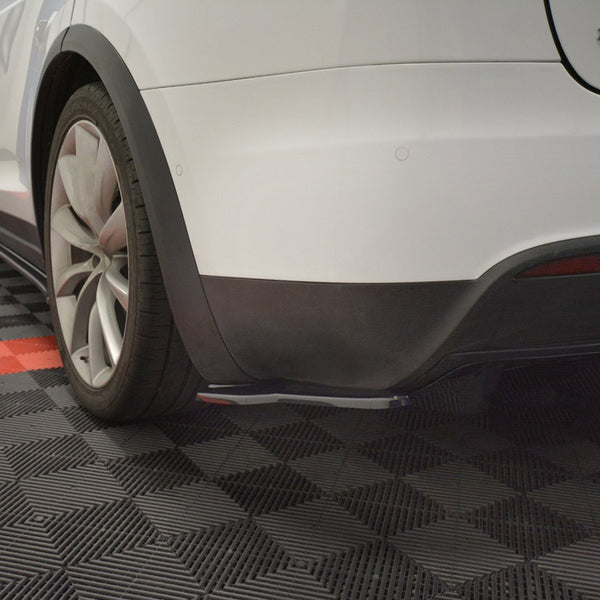 A white car's rear section is parked on a checkered black and red floor. The car is stationary, with visible rear wheels and fender. Text reads "MODEL" partially visible.