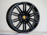A black alloy wheel, featuring a multi-spoke design and the Porsche emblem at the center, stands against a plain background, resting on a white surface.