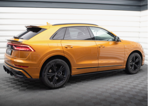 A metallic orange SUV is parked in a bright, white-walled showroom with a dark, textured floor, featuring sleek design and black alloy wheels.