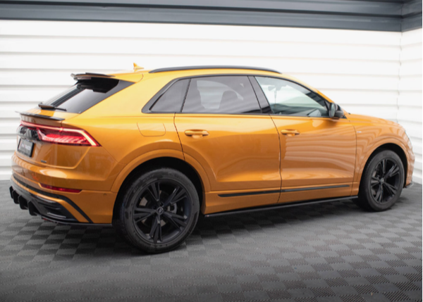 A metallic orange SUV is parked in a bright, white-walled showroom with a dark, textured floor, featuring sleek design and black alloy wheels.