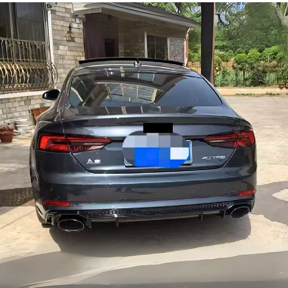 A dark-colored Audi A5 car is parked, rear view showing dual exhausts and "40 TFSI" badge, outside a brick house with a garden fence and trees in the background.