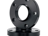 A black, cylindrical metal flange with a central hole and multiple peripheral holes is vertically stacked on a similar flange, set against a white background.