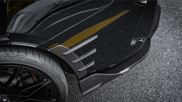 A car tire with a black alloy wheel is parked on asphalt. The vehicle features carbon fiber aerodynamic fins and a glossy black surface, reflecting a yellow line. Text: "MADE IN GERMANY RADIAL TUBELESS."