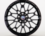 A glossy black alloy wheel with intricate geometric design, displaying the BMW emblem at its center. It is standing upright against a plain white background.