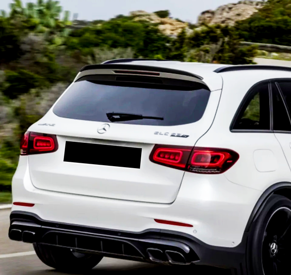 A white SUV drives on a road with surrounding greenery. Text on the vehicle reads "GLC 63S" and "AMG" near the Mercedes logo.