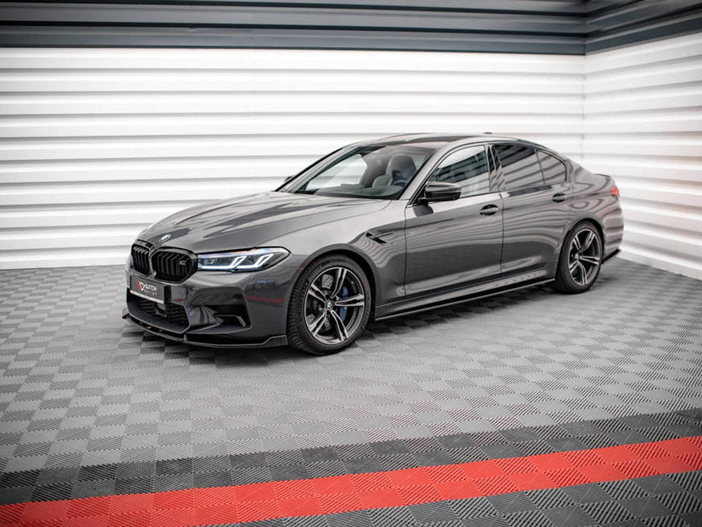 A sleek, gray sedan is parked on a patterned floor in a modern showroom with striped walls. The license plate reads "VATTEN EXKLUSIVE."