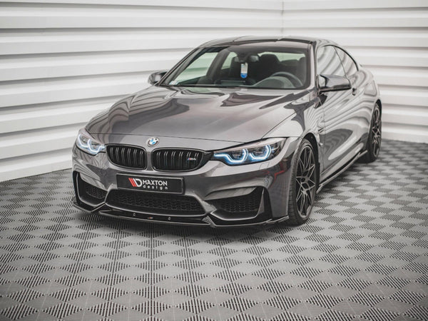 A sleek, gray BMW sports car with illuminated headlights sits on a checkered floor in a bright, white-paneled room. A license plate reads: "MAXTON design."