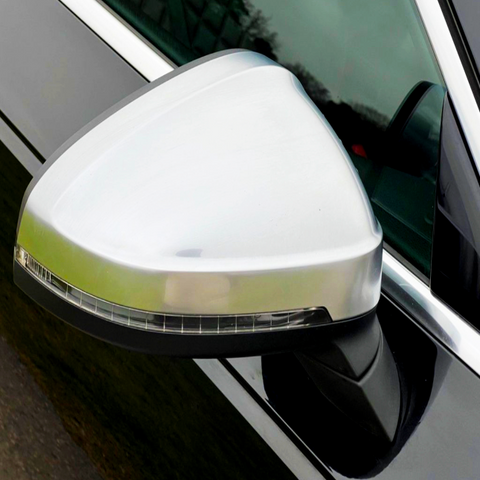 A silver car side mirror features an integrated turn signal, attached to a black vehicle door in daylight.
