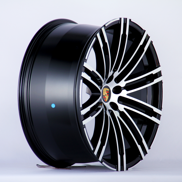 A glossy black and silver alloy wheel is angled to show its intricate spoke design, featuring a central emblem with the Porsche logo. The background is plain white.