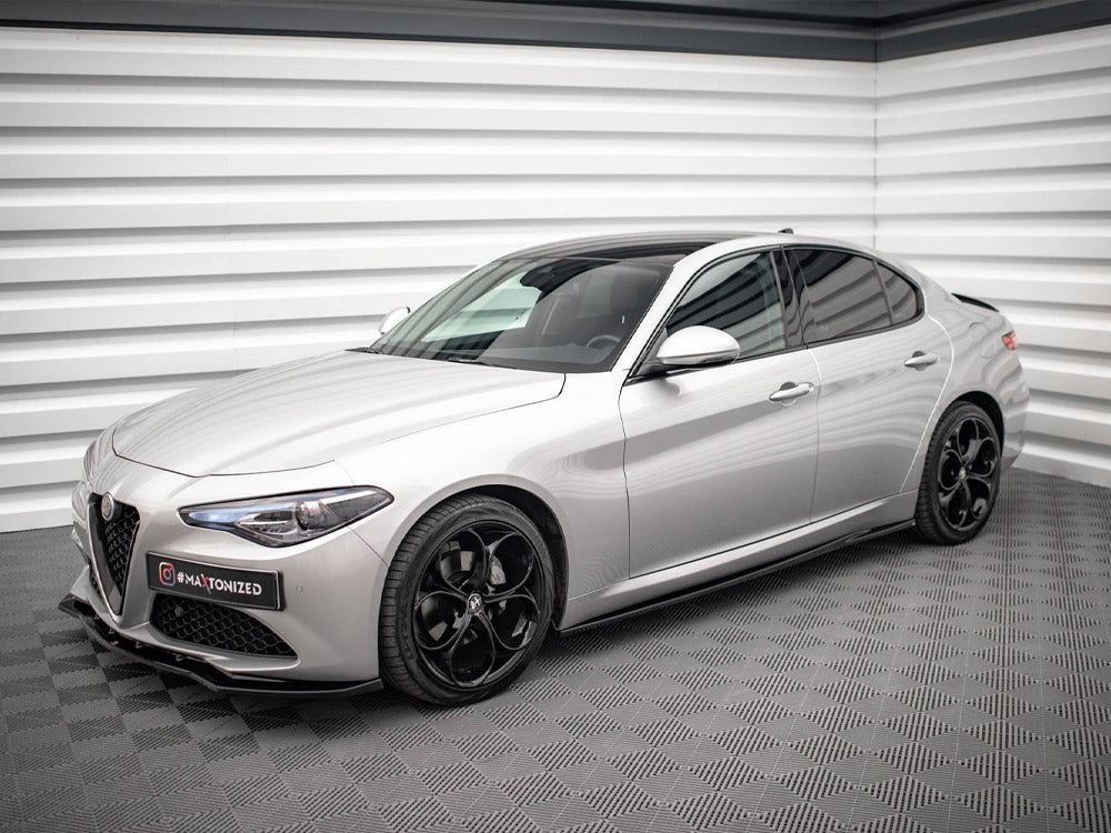 A sleek silver sedan is parked in a modern showroom with textured white walls and a patterned floor. A sign on the front reads "#MAXTONIZED".