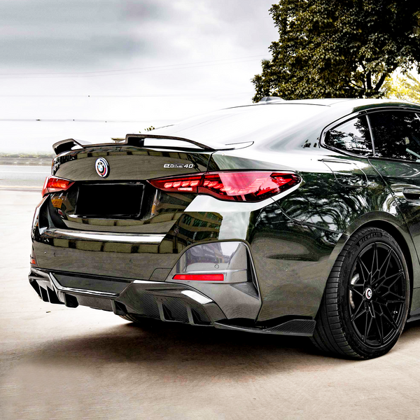 A sleek black car with a "b3x5 4D" badge is parked on a concrete surface, surrounded by trees and a cloudy sky.
